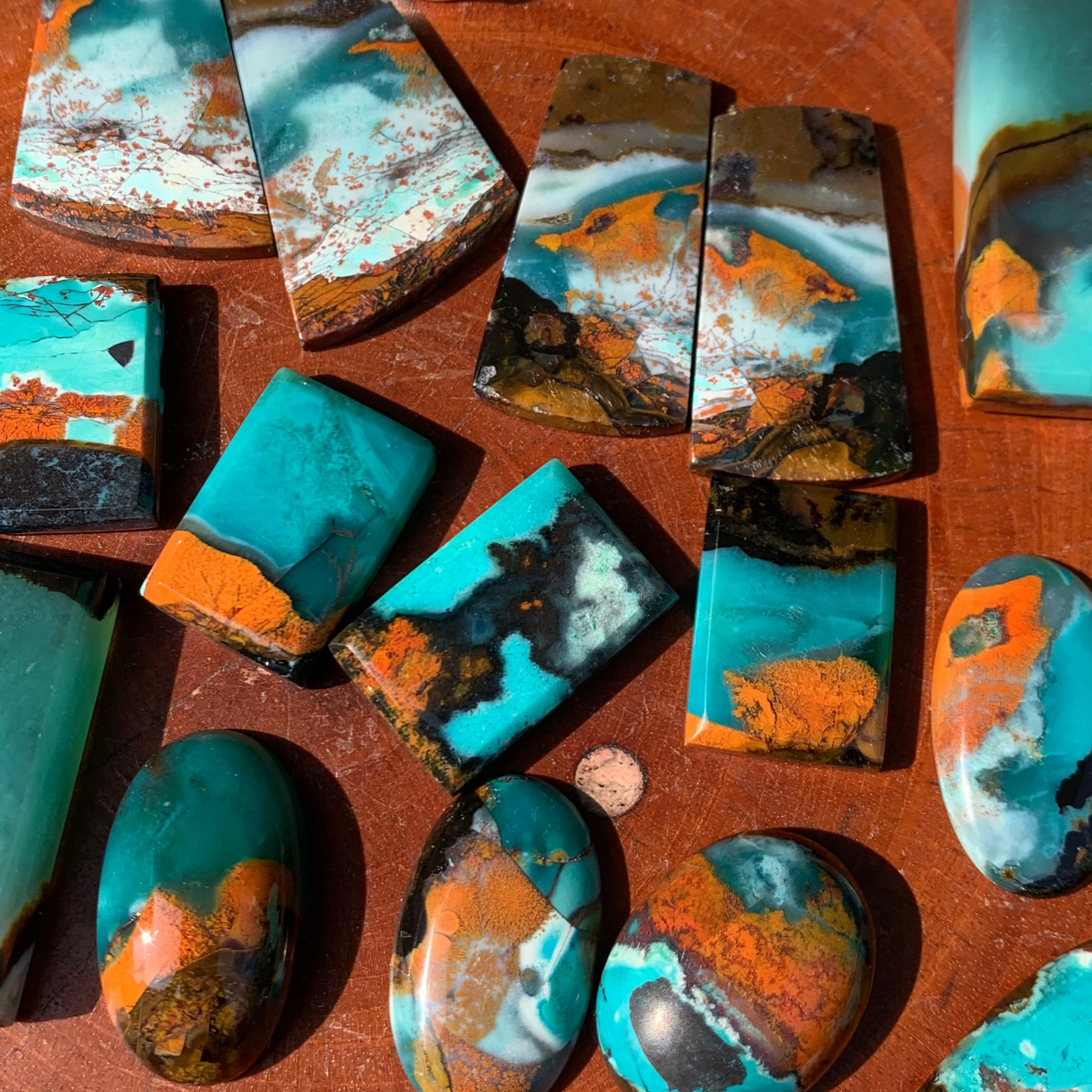 Collection of turquoise and orange stone pendants on a wooden surface with a business card in the background.